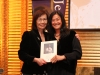 two women standing together holding plaque