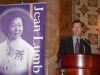 man speaking behind podium next to Jean Lumb banner