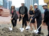 Several people in white construction hats digging into dirt.