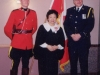 Jean in black judge robes standing with mountie police in front of Candian flag