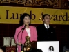 Arlene Chan and Stephen Wong speaking behind podium with balloons overhead and Jean Lumb banner in the background