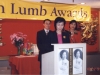 Women speaking behind podium with large Jean Lumb banner hung overhead