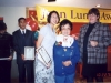 three people on stage with Jean Lumb banner in the background