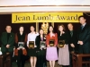 people grouped together onstage for a picture under Jean Lumb banner, four are holding their award plaques