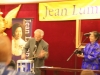 two musicians playing drum and cowbell quickly, they are on stage next to Jean Lumb banner