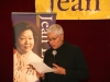 women reading off sheet of paper while holding a microphone
