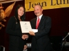 gentleman handing award to female award winner . They are shaking hands