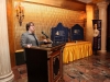 women speaking at podium with large plaques visible behind her