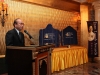 man speaking at podium with  large plaques visible behind him