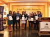 award winners standing in gold lobby with Jean Lumb foundation signs. They are grouped together and holding their plaques