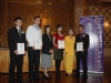 six award winners onstage holding their plaques next to Jean Lumb banner. Everyone is dressed for the formal occassion