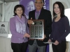 man holding plaque standing between two women