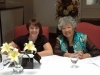 two women smiling while seated behind table to check in guests