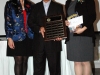 three people standing together for photo. Man in center is holding a plaque