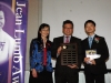 three people standing together for photo. Man in center holding plaque