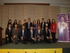 large group together on stage kneeling and standing next to Jean Lumb banner