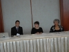 three people seated behind white table.