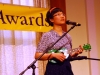 Musician playing green ukulele on stage.