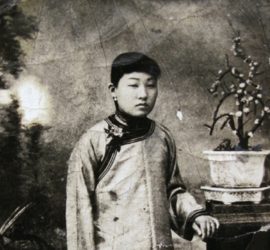 young chinese women in tradition attire standing next to small potted tree.