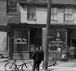two men talking outside a laundromat next to a telephone pole and bicycle