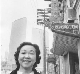 Black and white of Jean Lumb smiling in front of her chinatown restaurant